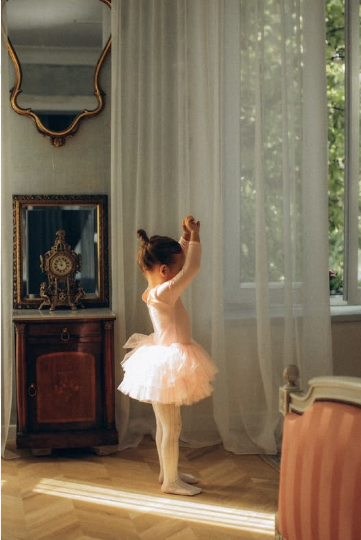 A young ballerina in a pink tutu standing in a sunlit vintage room